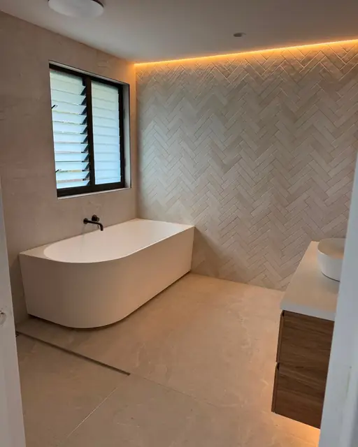 Freestanding bath beneath a louvre window with a rain shower alongside