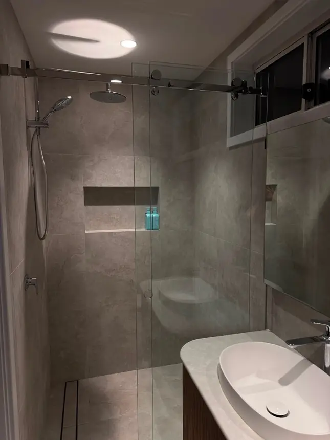 The finished bathroom with a frameless glass shower and a fluted timber vanity