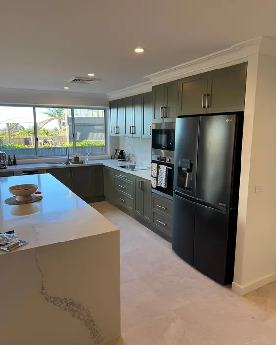 Kitchen with a stone island bench and deep green shaker cabinetry